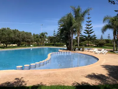 a large swimming pool with chairs and palm trees at Appt BOUZNIKA EDEN ISLAND pied sur Mer pour FAMILLE et Couple MARIE in Bouznika