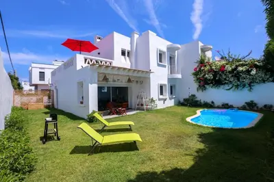 a white house with a yard with chairs and a pool at Chez Didier Tamaris Beach in Dar Bouazza