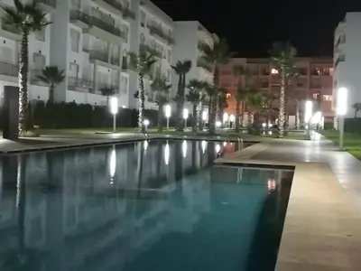 a swimming pool at night with palm trees and buildings at appartement Shems Bouznika Premium in Bouznika