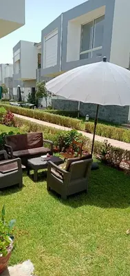 two chairs and an umbrella in the grass at Appartement Familial avec Jardin, Résidence avec Piscine Dar El Bahr in Sidi Rahal