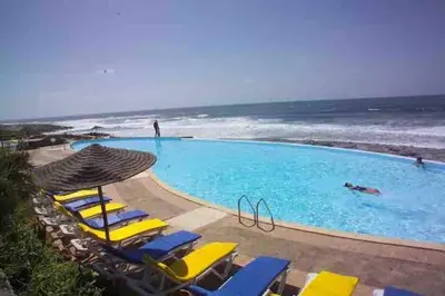 a swimming pool with yellow lounge chairs and the ocean at Appartement vue mer panoramique in Tamaris