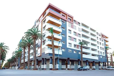 a tall building with palm trees in front of it at OceanParc - Vue sur Mer et Parc 24H Sécurité in Mohammedia