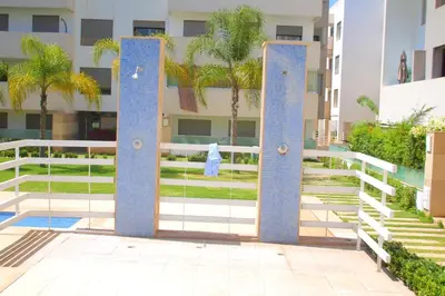a gate in front of a building with palm trees at Fermer Appartement dans résidence Paradis Beach in Mohammedia