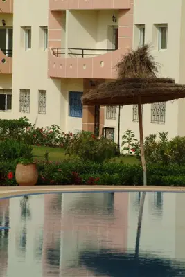 a pool with a straw umbrella and a building at MOHAMMEDIA Plage à 300m et piscine sur place in Mohammedia