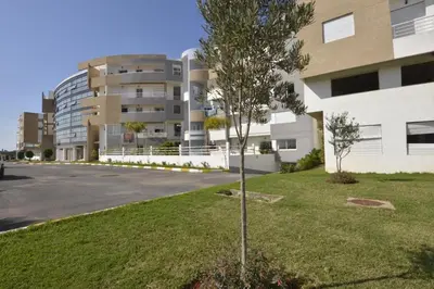 a tree in the grass in front of a building at BOUZNIKA Appartement avec piscine et plage à 3km in Bouznika