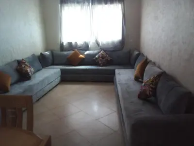 a living room with a blue couch and a window at BOUZNIKA Appartement avec piscine et plage à 3km in Bouznika