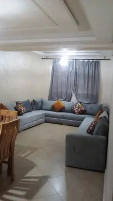 a living room with a blue couch in front of a window at BOUZNIKA Appartement avec piscine et plage à 3km in Bouznika