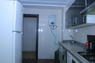 a white kitchen with a sink and a refrigerator at BOUZNIKA Appartement avec piscine in Bouznika