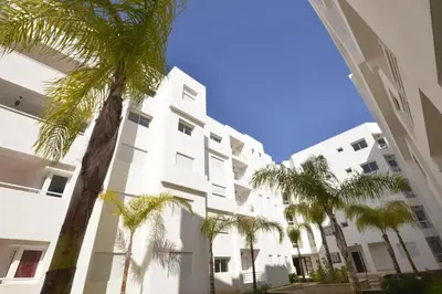 a white building with palm trees in front of it at BOUZNIKA Appartement avec piscine in Bouznika