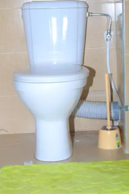 a white toilet in a bathroom with a brush at BOUZNIKA Piscine et plage in Bouznika
