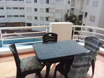 a table and two chairs on a balcony with a pool at Superbe appartement Bouznika in Bouznika