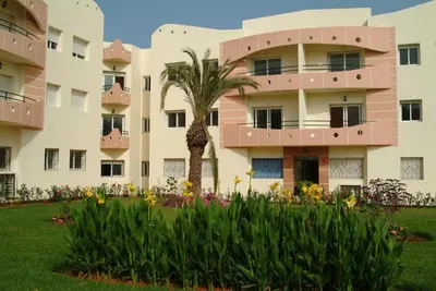 an apartment building with a palm tree and flowers at Les terasses de la mer Atlantique in Mohammedia