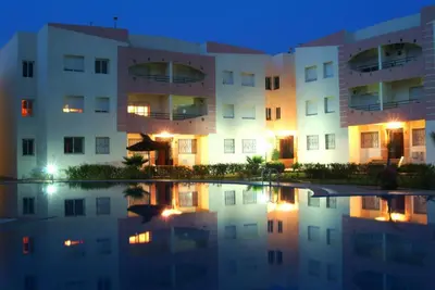an apartment building at night with its reflection in the water at Les jardins du soleil in Mohammedia