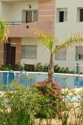 a house with a palm tree and flowers in front of it at MOHAMMEDIA Appartement avec 3 piscines et prés de plage in Mohammedia