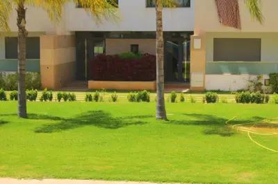 a lawn with palm trees in front of a building at MOHAMMEDIA L Oasis maritime in Mohammedia