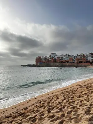 a sandy beach with buildings in the background and the ocean at bouzkina Costa beach golf in Bouznika