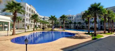 a swimming pool with palm trees and a building at bouzkina Costa beach golf in Bouznika