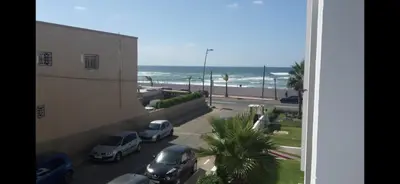 a view of a street with parked cars and the ocean at Appartement front de mer avec piscine en face des plages privées in Dar Bouazza