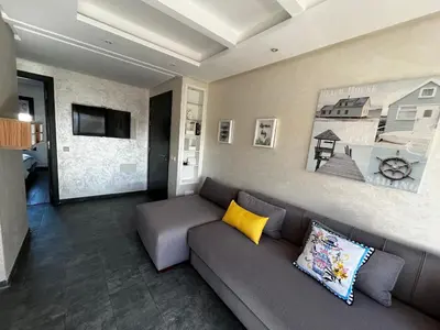 a living room with a gray couch and yellow pillows at Appartement front de mer avec piscine en face des plages privées in Dar Bouazza
