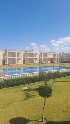 a building with a swimming pool and a tree in the grass at Bel appart à Hacienda Beach Sidi Rahal in Sidi Rahal