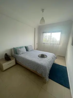 a bed in a white room with a window at Superbe appartement en résidence avec piscine in Sidi Rahal