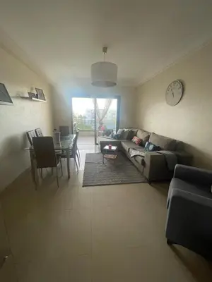 a living room with a couch and a table and a clock at Superbe appartement en résidence avec piscine in Sidi Rahal
