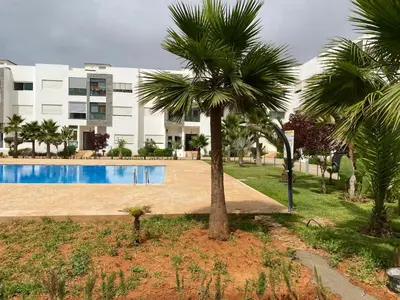 a palm tree and a swimming pool in front of a building at Lovely 4-bedroom condo with pool in Rabat