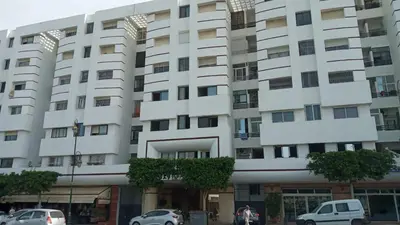 a large white building with cars parked in front of it at Bel Appartement spacieux 3 pièces avec double salon Paisible & Proche de la Gare d'Agdal in Rabat