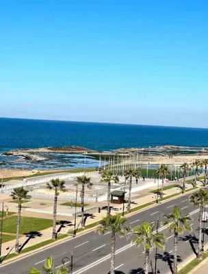 a street with palm trees and the ocean at Apartement sur la corniche, vue sur mer in Rabat