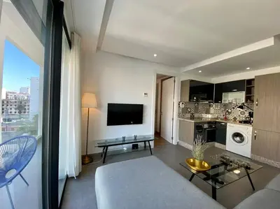 a living room with a couch and a tv and a kitchen at Racine Zara Street - By AppartAli in Casablanca
