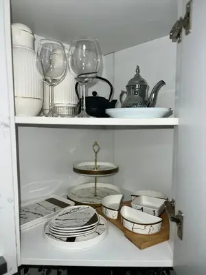 a white cabinet with dishes and wine glasses in it at Bel appartement avec une belle vue sur la grande mosquée Hassan II et la mer in Casablanca