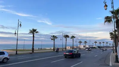 a street with cars driving down a road with palm trees at SUITOUISS - Océan 1 - Appartement centre ville au front de mer in Rabat