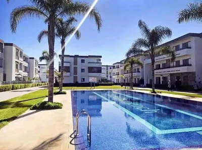a swimming pool with palm trees and buildings at Studio minimaliste marbella beach in Mansouria