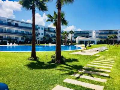 a swimming pool with palm trees in front of a building at Grand Apartement a Blanca Beach Sidi Rehal in Sidi Rahal
