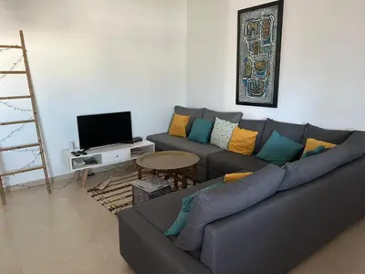 a living room with a couch and a television at Les Portes de l'Océan avec piscine uniquement l'été in El Harhoura