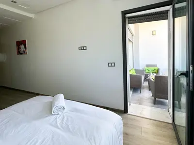 a bedroom with a white bed and a living room at luxe appartement met zeezicht en zwembad Mohammedia Parc in Mohammedia