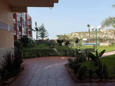 a brick walkway in a park with palm trees and a building at Appartement avec piscine proche de la plage in Mohammedia